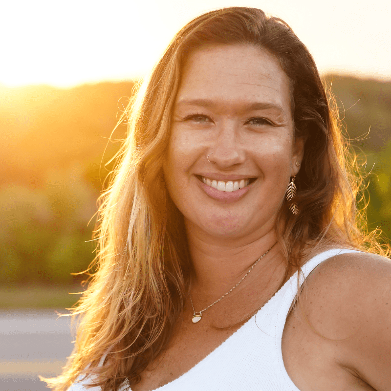 A woman (Tiffany Martin, midwife) is smiling at the camera, with a sun setting behind her.